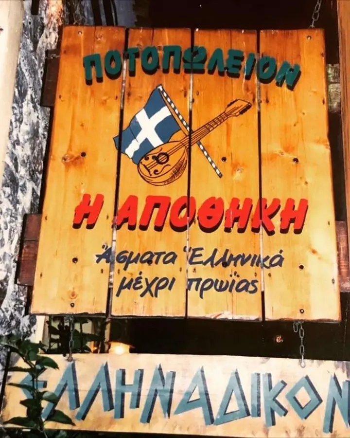 Η παλιά πινακίδα: «Ποτοπωλείον Η Αποθήκη — άσματα ελληνικά μέχρι πρωίας»
